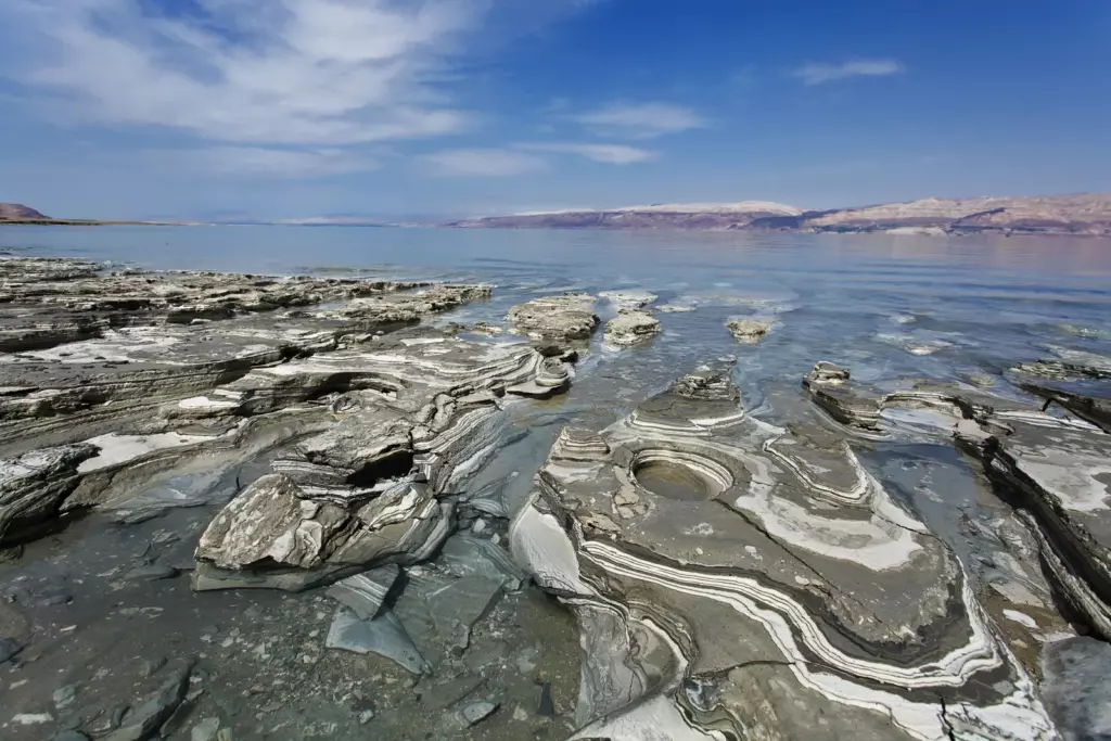 Dead Sea — Lines left by the water Layered pale salt formations and dark rocks beside the Dead Sea